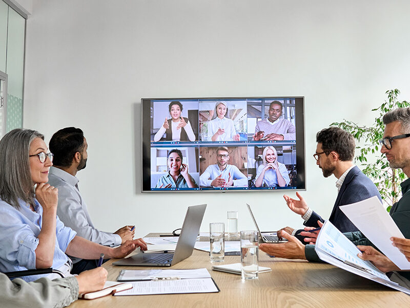 Diverse employees on online conference video call on tv screen in meeting room.