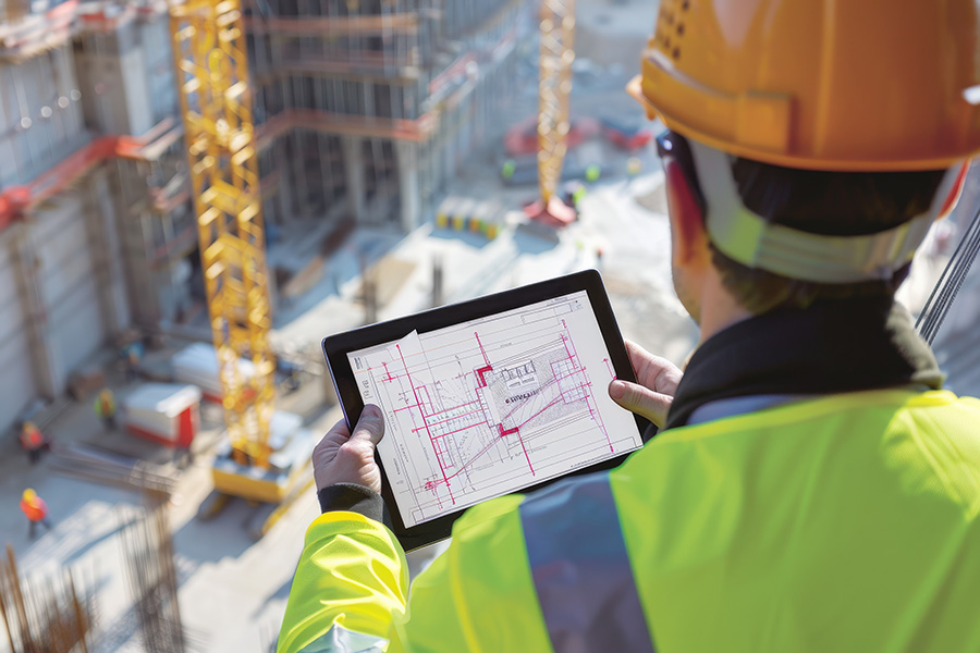 Construction worker wearing a hard hat and safety vest, looking at ipad